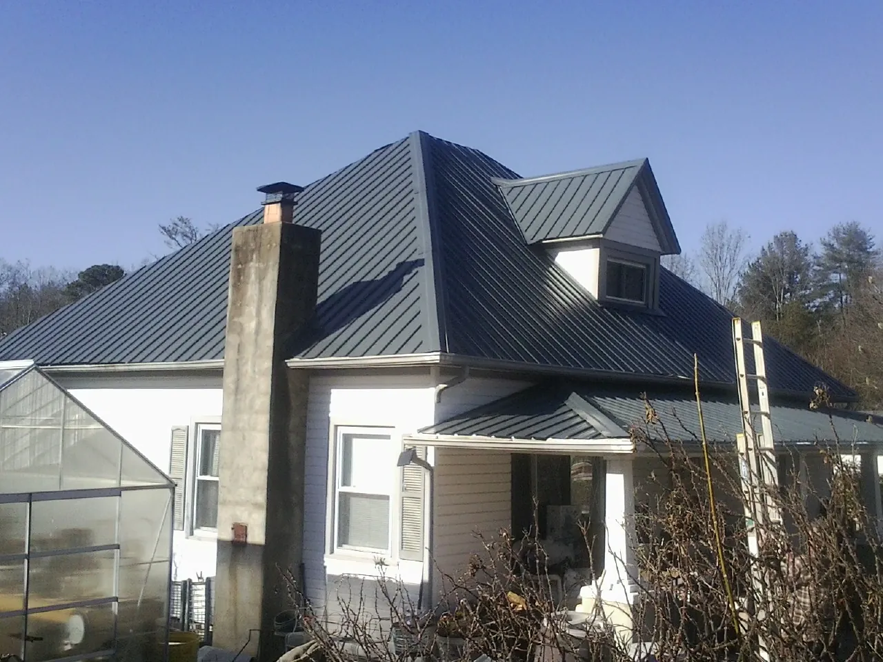 Dark blue standing seam metal roof on a white farmhouse with dormer — Slate & Tile Roof Repair by Roofing Brothers in Johnson Creek