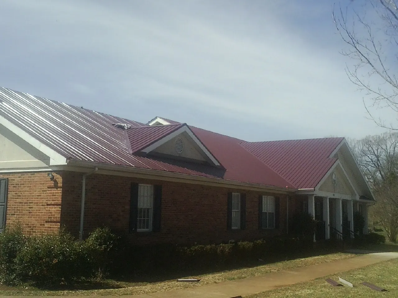 Red metal roof with gabled entries on a long brick building, from a Hail Damage Roof Repair job in Johnson Creek