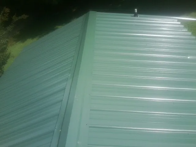 New green metal panels meeting at the ridge of a roof — Flat Roof Repair work by our crew in Johnson Creek