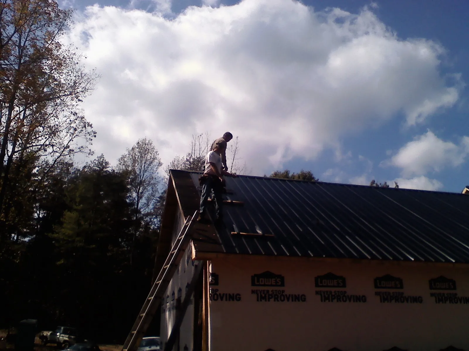 Roofer fastening dark metal panels high against a cloudy sky, from a Roof Inspection job in Johnson Creek