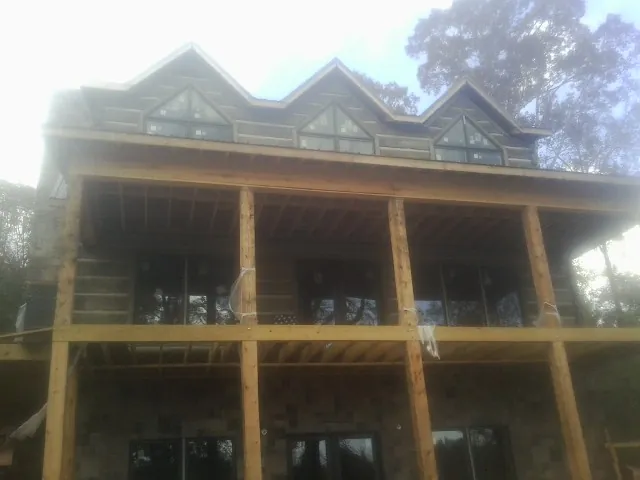 Dormers and porch framing on a large log home under construction — Roof Coating work by our crew in Johnson Creek