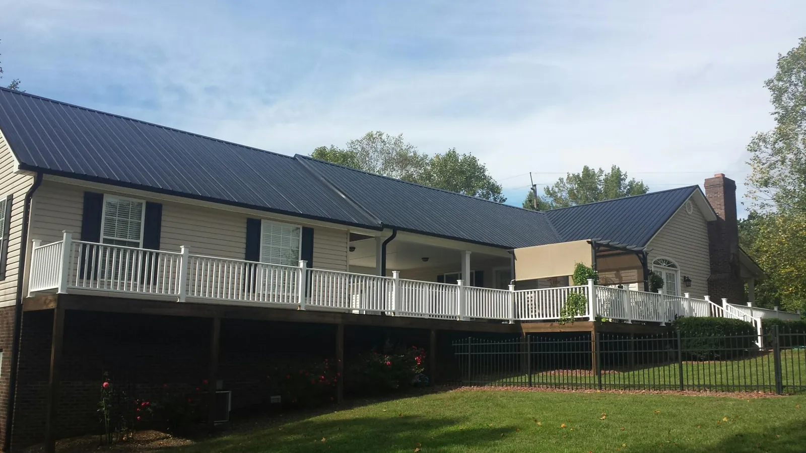 Black metal roof above a long white railed deck on a hillside home in Johnson Creek