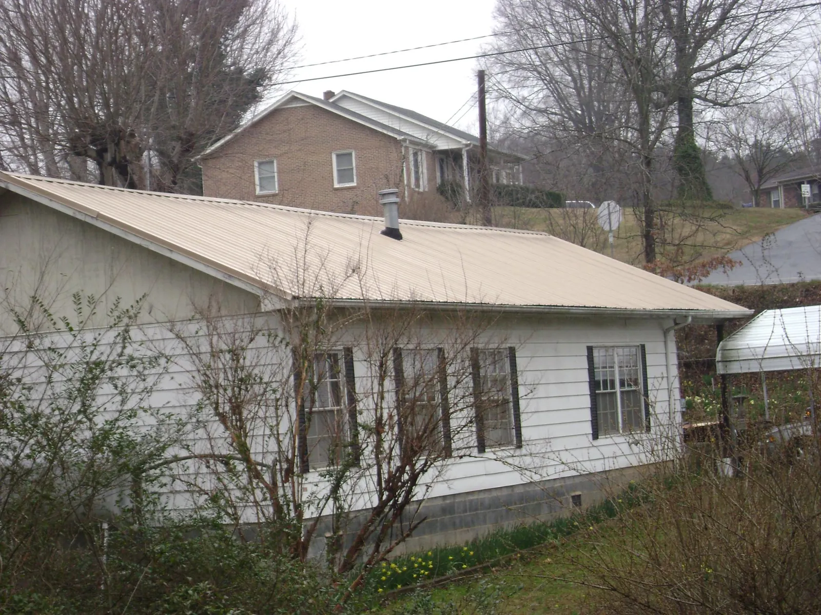 Tan metal roof on a white sided house set into a hillside — Commercial Roofing by Roofing Brothers in Johnson Creek