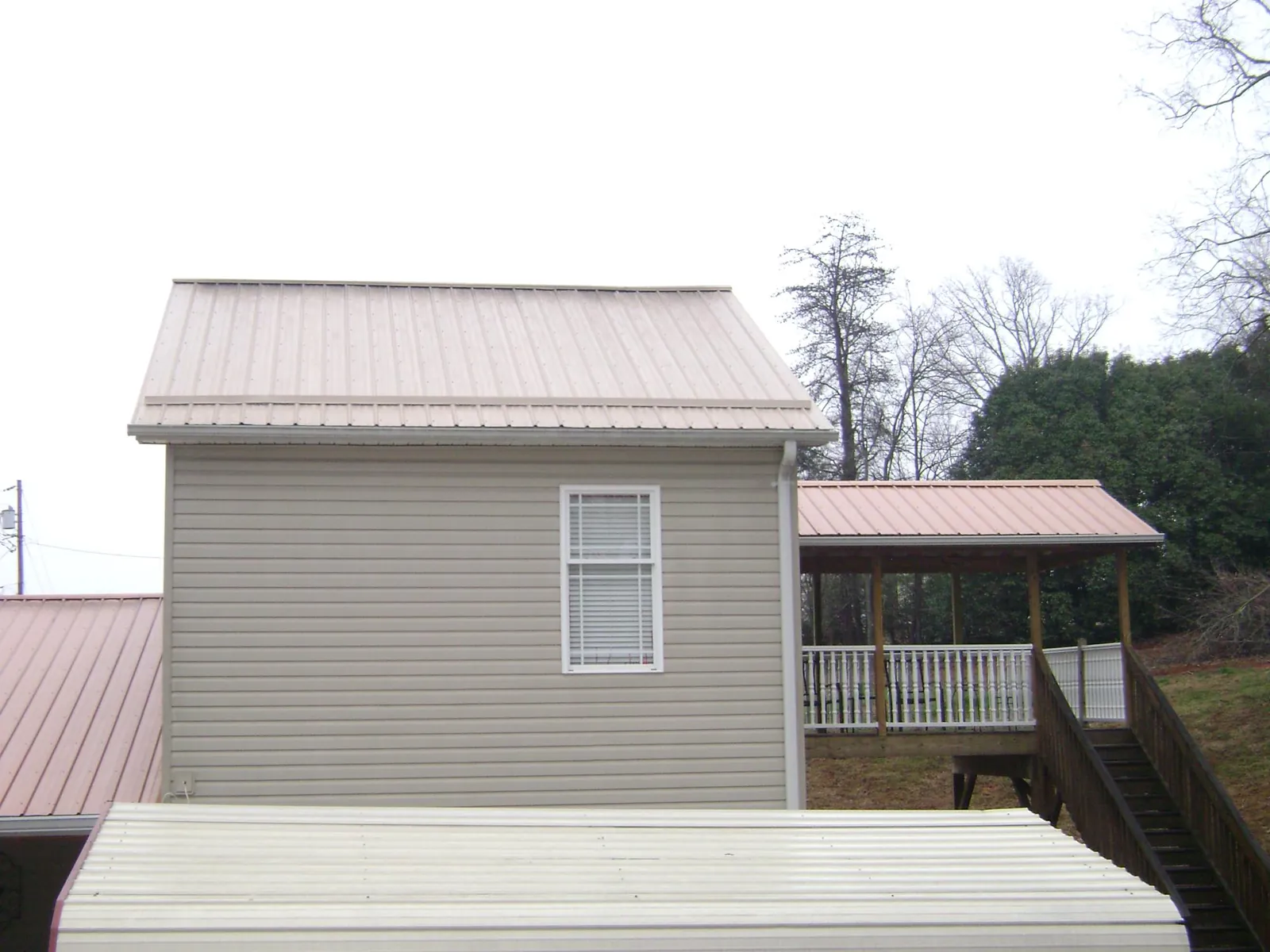 Tan metal roofs on a two story addition and attached porch, from a Roof Replacement job in Johnson Creek